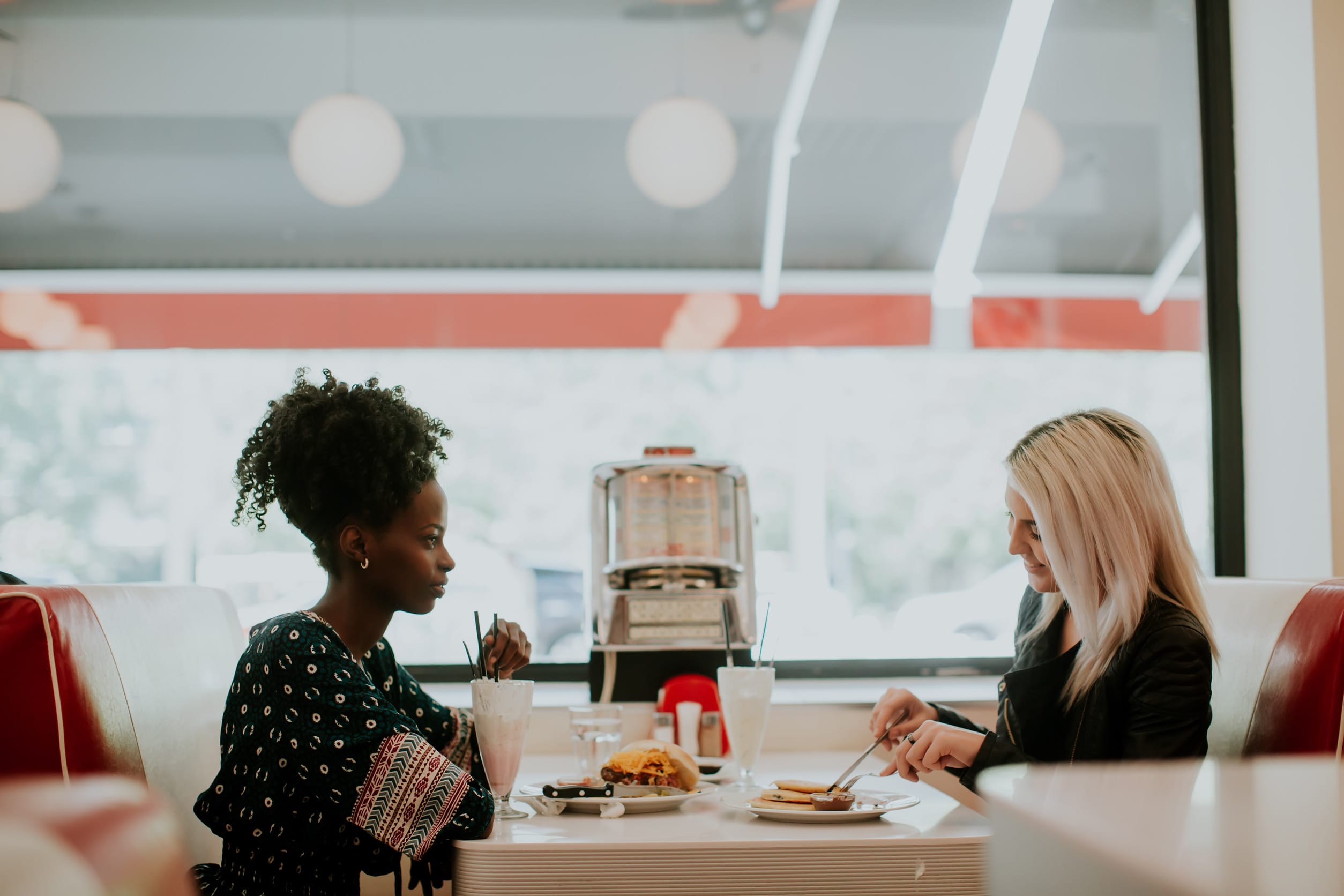 Multiracial female friends eating fast food at a table in the di 24-hour restaurants