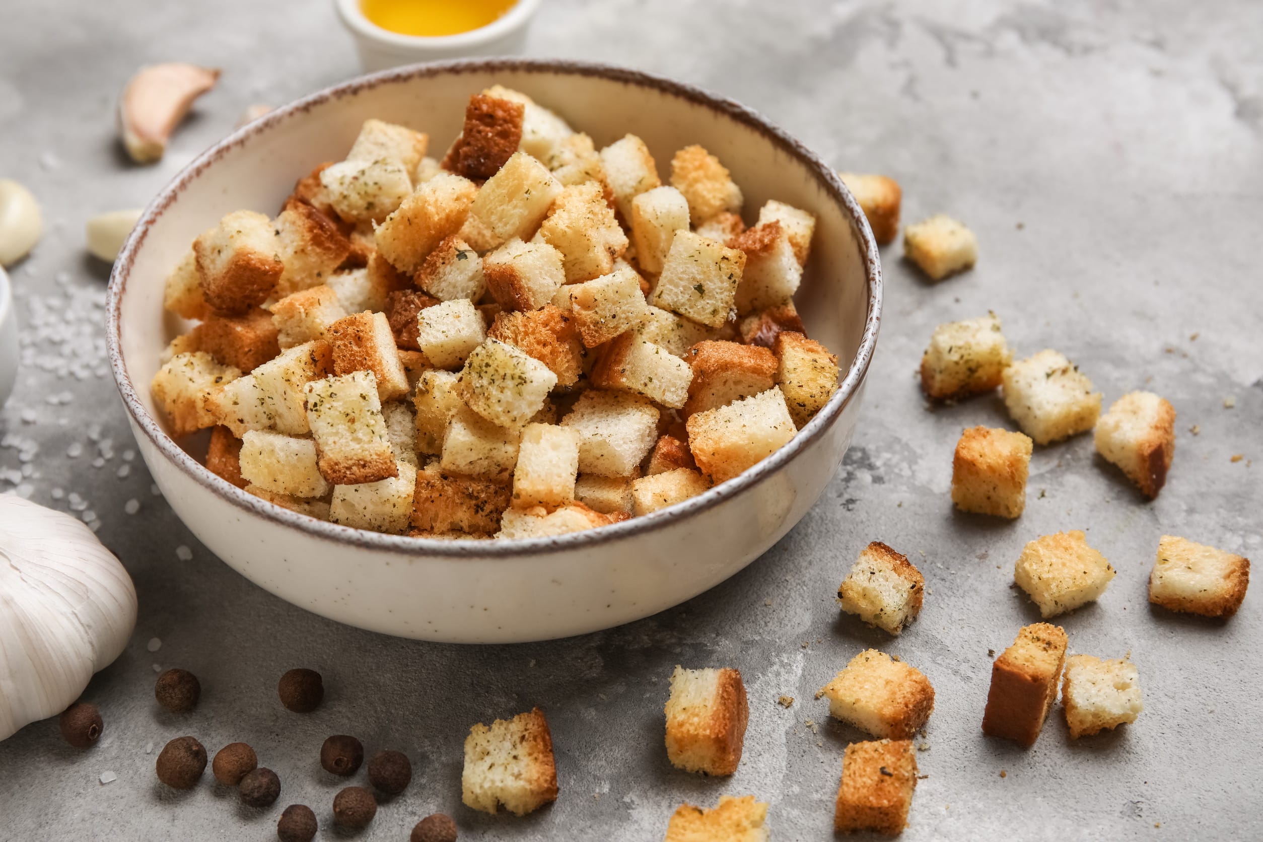 Bowl with crunchy croutons, peppercorns and garlic on grey background, closeup grocery store items