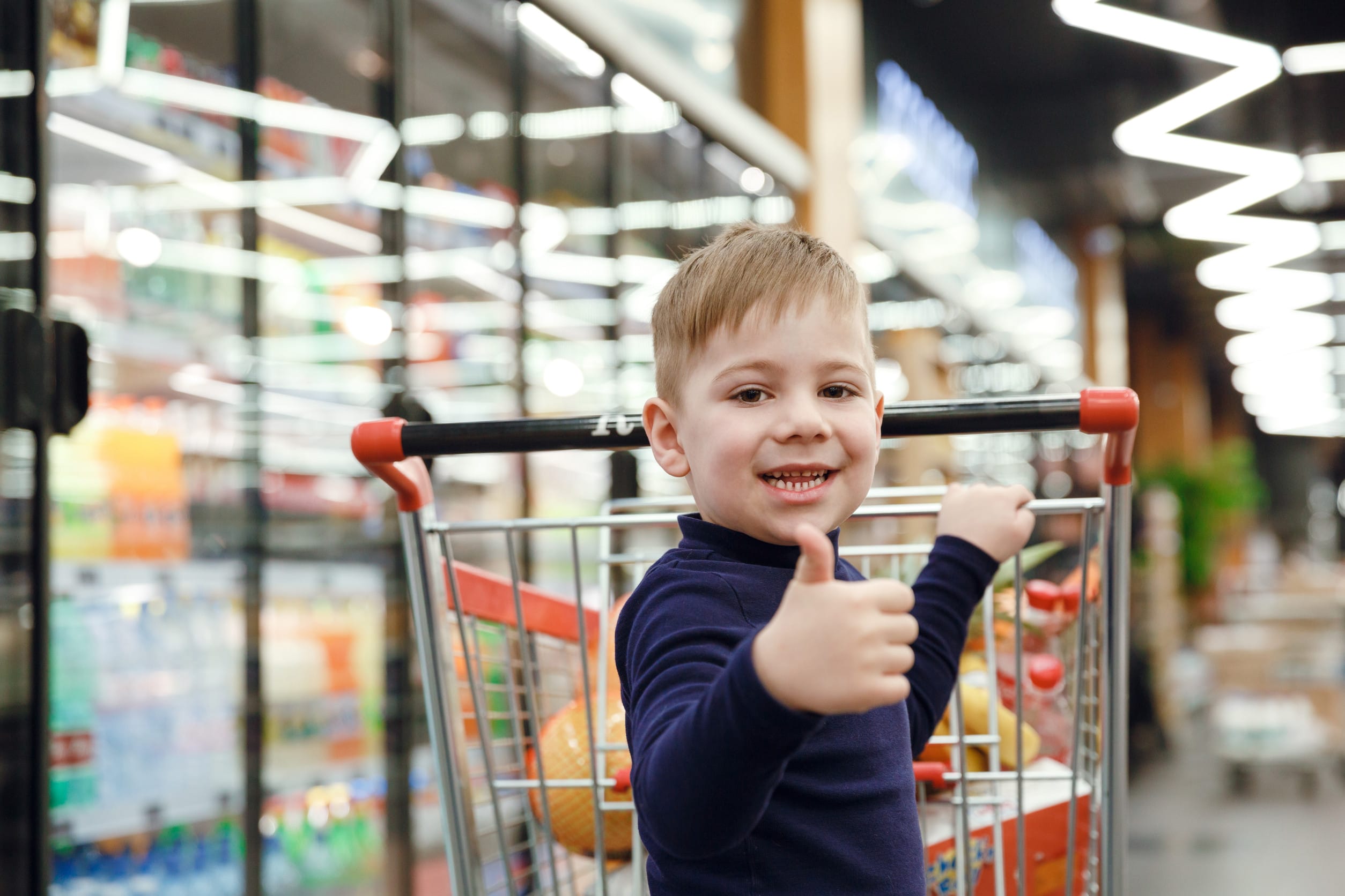 Happy boy near shopping trolley showing thumb up unsupervised purchases