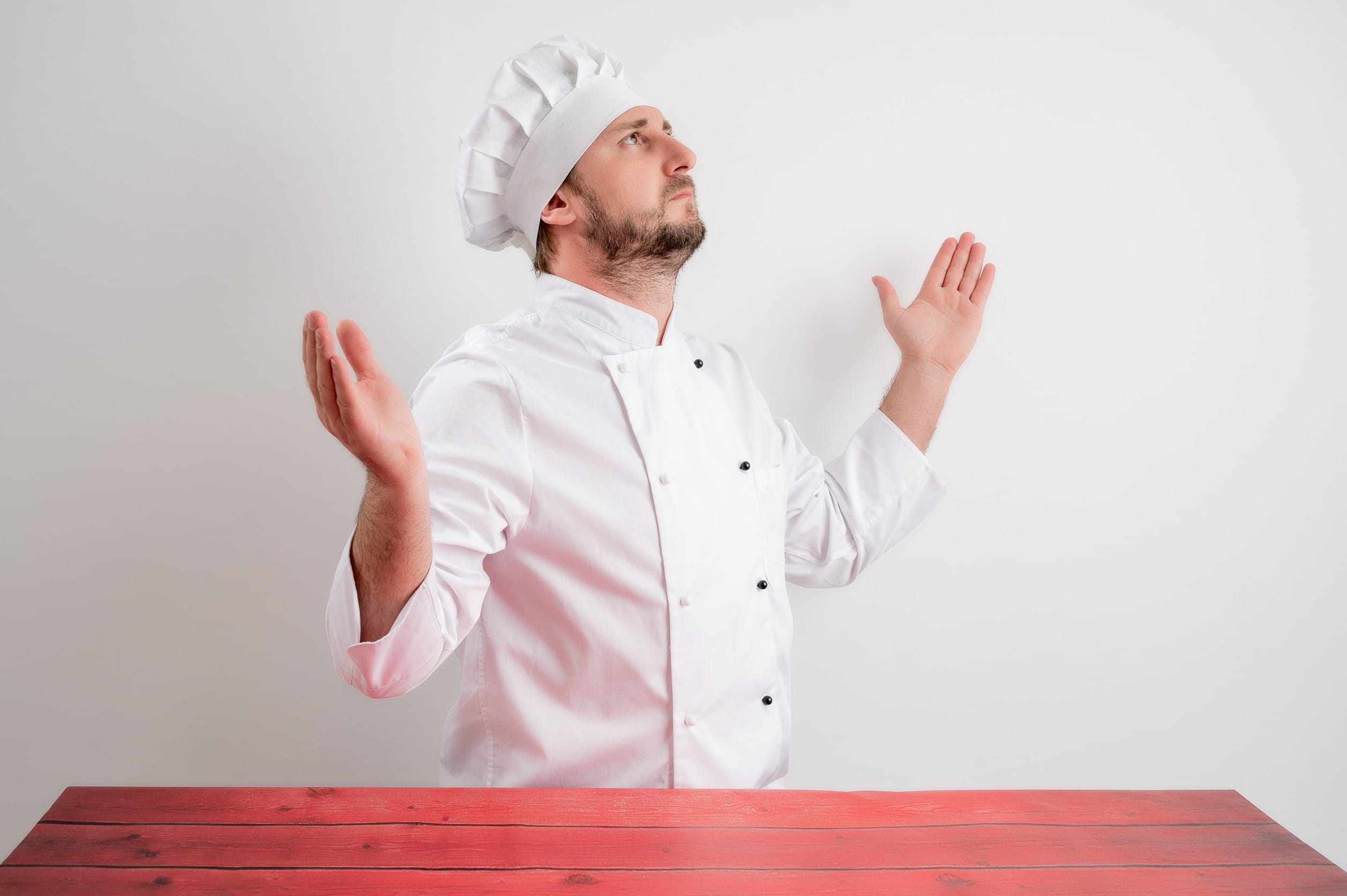 Young male chef in white uniform with open arms looking up, side confusing cooking instructions