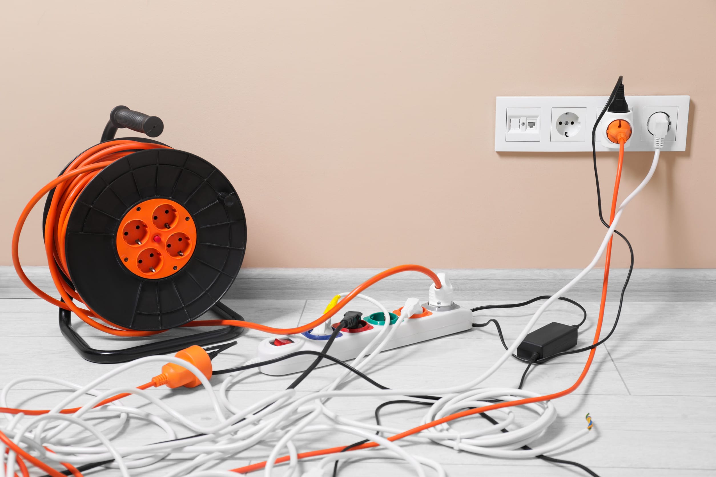 Extension cord reel plugged into socket on white floor indoors. outdated warning labels